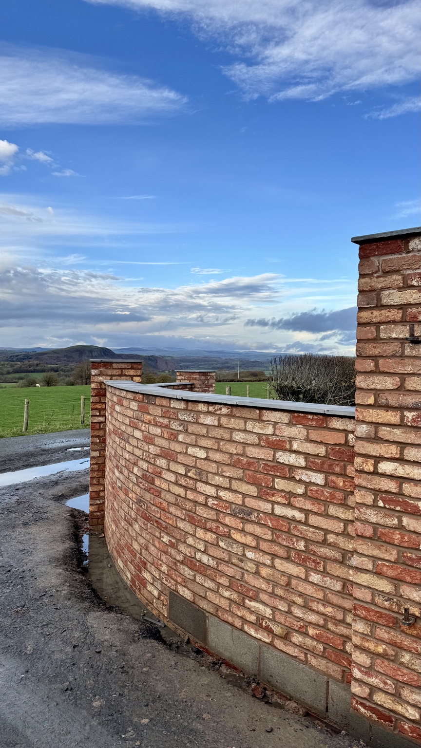 Curved brick entrance wall following the rural landscape
